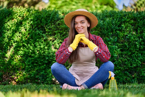 緑豊かな茂みの背景に緑の庭でわら帽子 エプロンと黄色のゴム手袋を身に着けている幸せな笑顔の女性の庭師の肖像画 — ストック写真