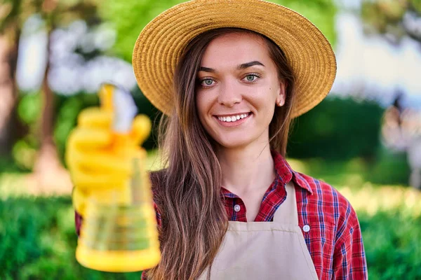 幸せな笑顔の肖像画晴れた日に庭の植物に散水するための黄色のスプレーボトルとわら帽子の魅力的な女性庭師 — ストック写真