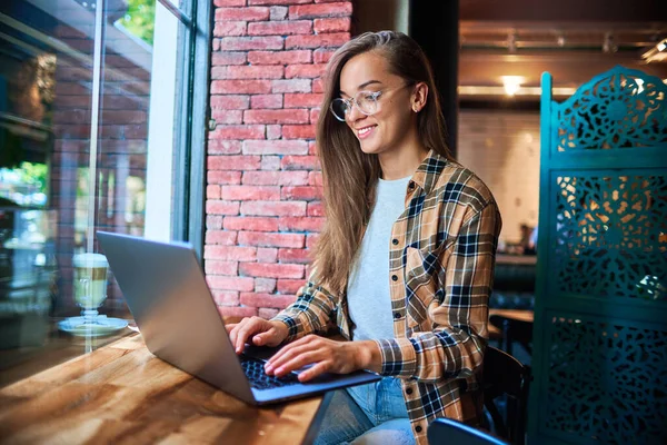 年轻而聪明的现代女性自由职业者 戴着眼镜 在咖啡店的笔记本电脑上远程工作 舒适的工作场所 — 图库照片