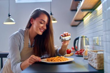 Gülümseyen mutlu genç aşçı kadın şef akşam yemeği için yemek hazırlar ve tuzlar.