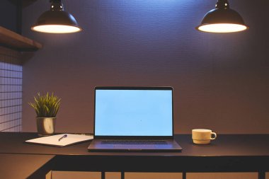 Modern bir çatı katında boş beyaz ekran modeli olan bir dizüstü bilgisayarda uzak çevrimiçi çalışma alanı