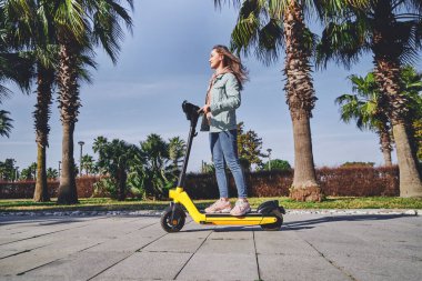 Genç, gündelik, modern, aktif, modern bir kadın şehirde gezmek için elektrikli scooter kullanıyor.    