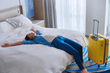 Otele giriş yaptıktan sonra otel odasındaki bir yatakta uzanan mutlu gezgin kadın. Tatilin ve tatilin tadını çıkar. Mutlu an