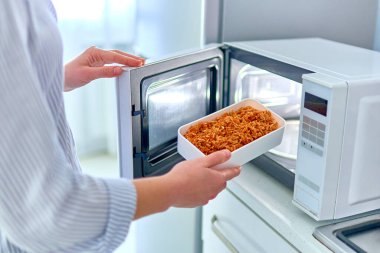 Kadın elleri, modern mikrodalga fırında yemek kabını ısıtıyor. Evde atıştırmak için. 