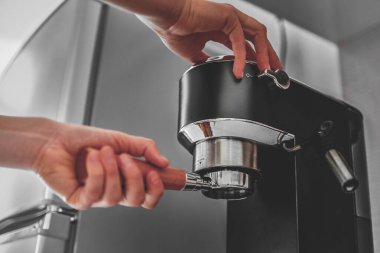 Kadın eli portafilter tutuyor ve modern bir kahve makinesi kullanarak evde taze aromatik kahve yapıyor. 