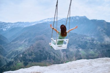 Özgür kadın gezgin, kolları açık salıncakta sallanmanın ve dağ manzarasının tadını çıkarıyor. Sakin ve sessiz yolculuk konsepti bir insanın mutluluğu ve özgürlüğü hissettiği an.