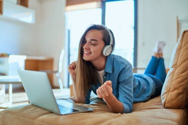Gündelik akıllı, modern gülümseyen milenyum kızı. Kapalı gözlü, kablosuz kulaklık ve laptop kullanan, evdeki kanepede dinlenirken müzik dinlemenin keyfini çıkaran. 