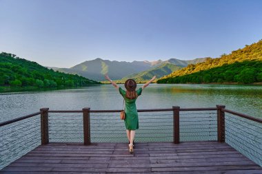 Kolları açık gezgin kız rıhtımın kenarında tek başına durup göle ve dağlara bakıyor. Güzel, mutlu bir özgürlüğün tadını çıkarıyorum. Hayat ve huzur dolu, sakin, huzurlu bir atmosfer. Arka plan