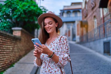 Mutlu gülümseyen, güzel, neşeli, genç kız gezgin tatilde gezerken akıllı telefon kullanıyor. 