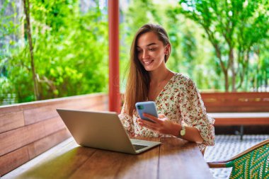 Mutlu, güler yüzlü, güzel, neşeli, genç, mutlu milenyum kızı bilgisayarını ve telefonunu uzak iş için kullanıyor, sosyal ağlar kuruyor ve Green Cafe 'de internette geziniyor. 