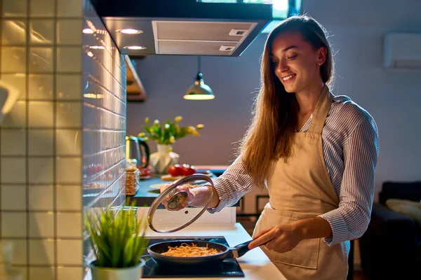 로프트식 주방에서 식사를 오븐에 올려놓은 프라이팬에서 요리를 매력적 행복하게 미소짓고 — 스톡 사진