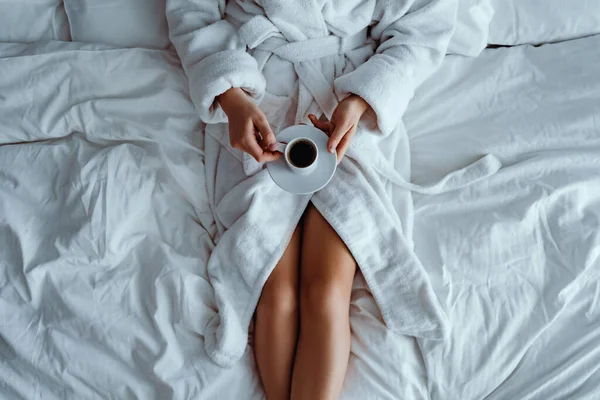 バスローブを着た怠惰な女性がベッドの上に横たわっており ホテルの部屋で居心地の良い快適なベッドルームでリラックスしている間に芳香族コーヒーカップを楽しんでいます 簡単な生活 新しい一日の始まり — ストック写真
