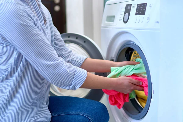 Woman housewife loads washing machine with dirty colored clothes at laundry day
