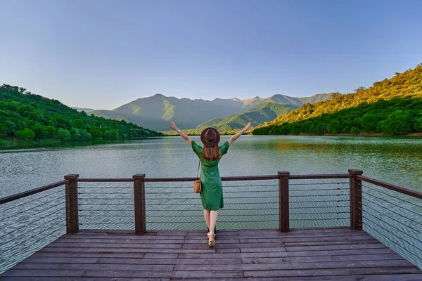 桟橋の端に一人で立って立ち上がり 湖や山を見つめ開いている旅行者の女の子 美しい幸せな自由の瞬間の生活と自然の中で穏やかな静かな静かな平和的な雰囲気をお楽しみください バックビュー — ストック写真