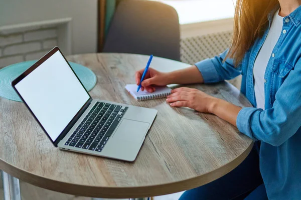 女性的手拿着笔在笔记本上记笔记 在笔记本电脑上工作 在工作空间的桌子上空白处显示 网上网站广告的计算机模拟 — 图库照片