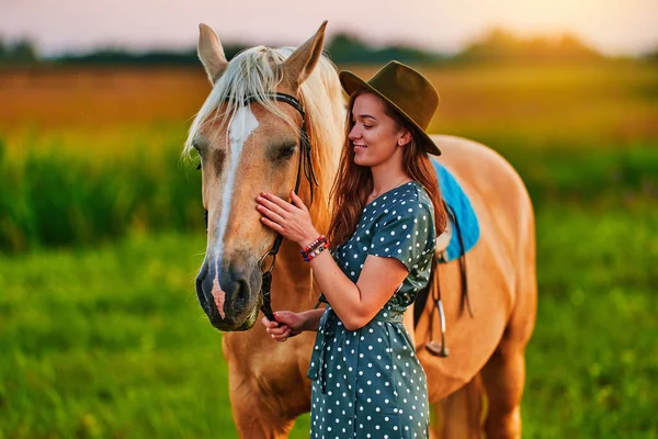 若いです可愛いです幸せな満足笑顔女性抱擁とストローク美しいですブロンドPalomino馬で牧草地で日没 — ストック写真