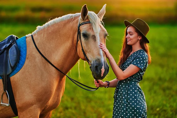 stock image Young cute happy joyful satisfied smiling woman hugging and stroking beautiful blond palomino horse at meadow at sunset