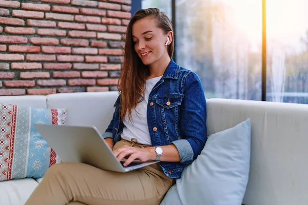 かわいい若い幸せな笑顔の女性は リモートワーク ブラウジング オンラインビデオの視聴 カフェでのチャットやソーシャルネットワークのためのラップトップを使用して白いヘッドフォンを身に着けています — ストック写真
