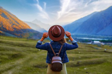 Tek başına seyahat eden şapkalı ve sırt çantalı kadın yolcuların arka görüntüsü. Gürcistan 'daki dağ vadisine kaçmak