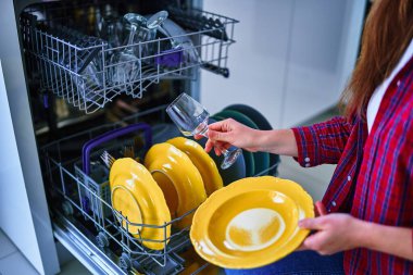Ev hanımı, modern bulaşık makinesini ev mutfağında bulaşık ve bardak yıkamak için kullanıyor. 