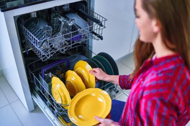 Ev hanımı, ev mutfağında bulaşık ve bardak yıkamak için modern bulaşık makinesi kullanıyor.