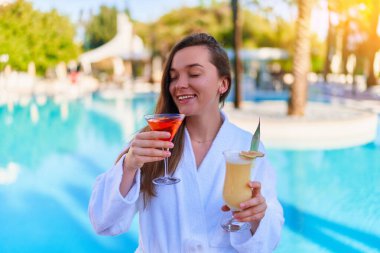 Young happy smiling joyful woman enjoy of summer vacations with refreshing pina colada and aperol cocktails by the pool at the all-inclusive resort 