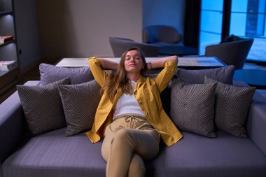 Sakin sakin kız hayalperest elleri başının arkasında yalnız başına kanepede dinleniyor. 