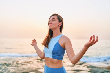 Mutlu bir fitness kadını. Gözleri kapalı. Meditasyon pozisyonunda elleri ve nefes egzersizleri ile tek başına duruyor. Zihinsel bakım ve sağlıklı alışkanlıklar