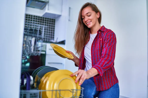 若い幸せ満足笑顔かわいい主婦女性使用現代食器洗い機用食器洗い機とメガネのための白い家庭用キッチン — ストック写真