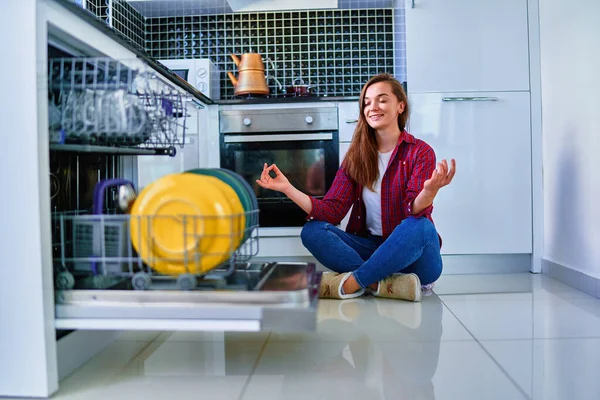 白い家庭のキッチンで食器洗い機やメガネのための近代的な食器洗い機を使用して若い幸せな主婦の女性 掃除中はリラックスしてお楽しみください — ストック写真