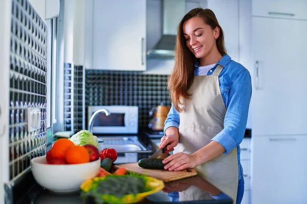若い幸せな幸せな幸せな笑顔の主婦準備と健康的な食事のための新鮮なベジタリアンサラダのための板に熟した野菜をカット — ストック写真