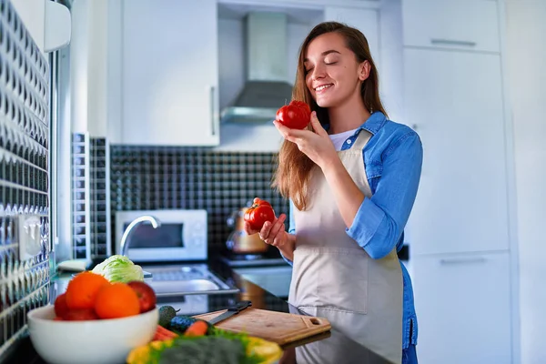 若い幸せな幸せな喜びかわいい笑顔主婦身に着けているエプロン準備新鮮なベジタリアンサラダ健康的な食事のために自宅キッチン — ストック写真