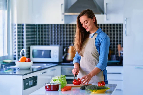 若い幸せな幸せな幸せな笑顔の主婦準備と健康的な食事のための新鮮なベジタリアンサラダのための板に熟した野菜をカット — ストック写真
