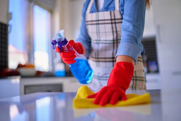 エプロンと赤い保護ゴム手袋を身に着けている主婦はスプレーボトルとラグを使用してほこりテーブルを拭くと消毒 — ストック写真