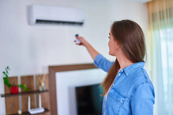stock image Female adjusting temperature of air conditioner on remote control at home in the living room