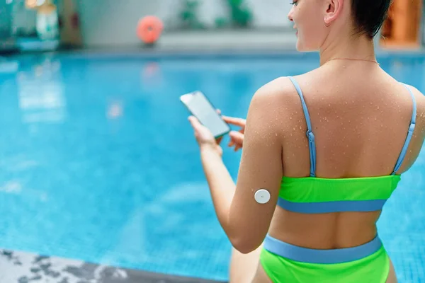 Active athletic fitness diabetic patient monitoring glucose level with remote sensor while training at swimming pool. Smart medical technology in diabetes treatment. Copy space