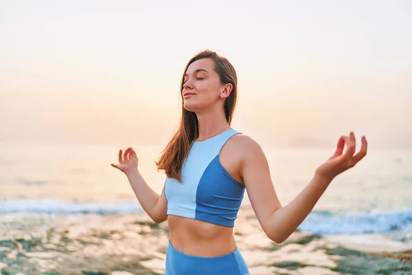 Blissful one fitness woman with closed eyes standing alone with meditation position hands while breathing exercises. Mental mind care and healthy habits