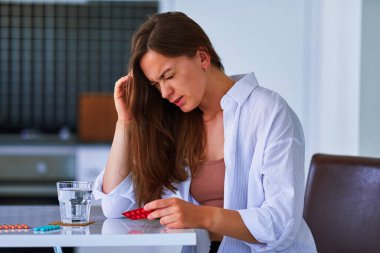 Sağlıksız, baş ağrısı çeken ve elinde ağrı kesici haplarla gezen ağrılı bir kadın. Sağlık sorunları