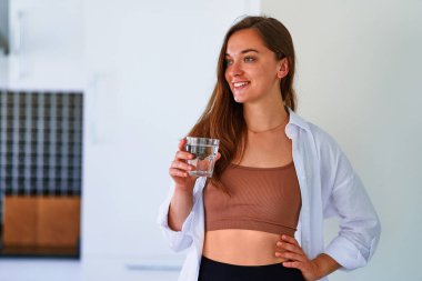 Mutlu genç ve güzel bir kadının portresi bir bardak saf su içiyor. Sağlıklı günlük alışkanlıklar ve su dengesini desteklemek 
