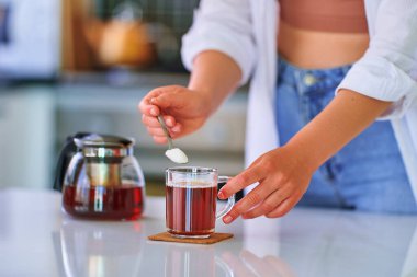 Kadın elleri sıcak siyah çayla cam bardağa şeker kaşık döküyor.