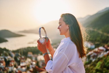 Mutlu, sakin, gözleri kapalı, günbatımında güzel manzaralı sakin müzik dinlemekten zevk alan bir kadın. Rahatlama stresi ve sağlıklı zihinler 