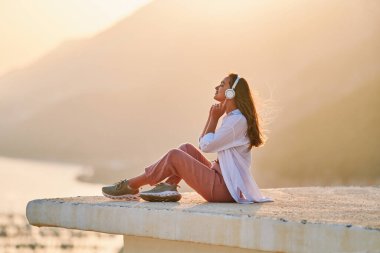 Mutlu, sakin, gözleri kapalı, günbatımında güzel manzaralı sakin müzik dinlemekten zevk alan bir kadın. Rahatlama stresi ve sağlıklı zihinler 