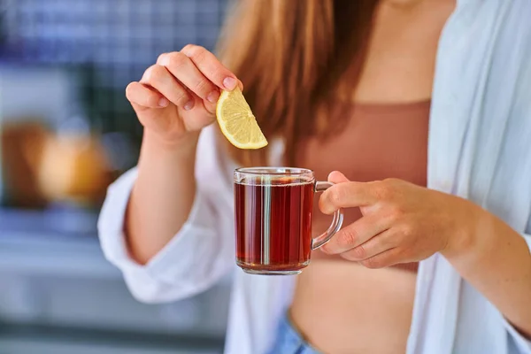 女性飲む熱い紅茶とともにレモンスライスでホームキッチン — ストック写真