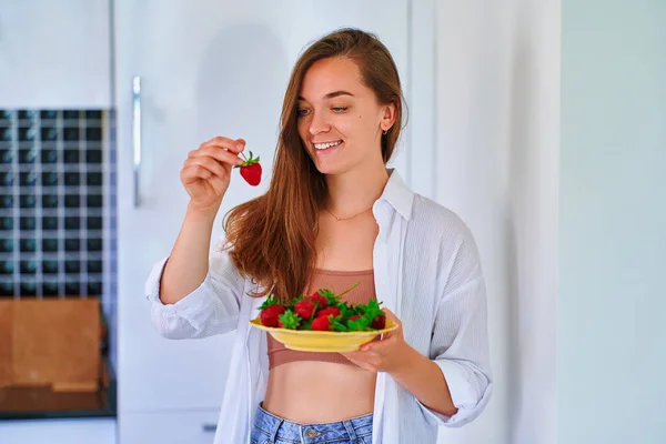 在家里厨房里吃新鲜成熟草莓的漂亮而快乐的快乐的小女孩 — 图库照片