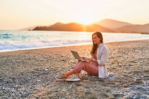 stock image Happy smiling cute joyful satisfied girl freelancer remote working online on the seashore at sunset time. Work everywhere