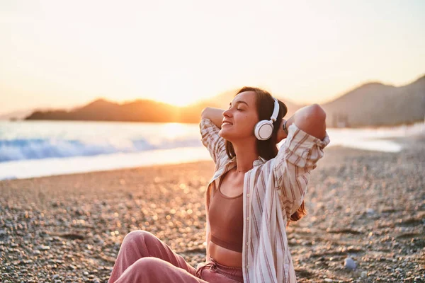 宁静而孤独的女人 闭着眼睛 喜欢听音乐 在日落时分 放松在海滨旅行的音乐 快乐美丽的生活 — 图库照片
