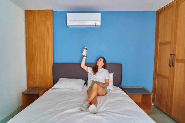 침대에 미소짓는 귀여운 침실에서 리모컨을 사용하여 에어컨의 온도를 조절하는 — 스톡 사진