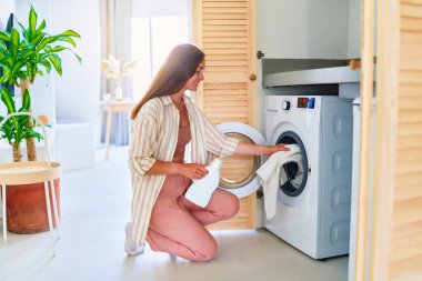 Güzel, sevimli, mutlu, mutlu, güler yüzlü ev kadını evde çamaşır yıkıyor.