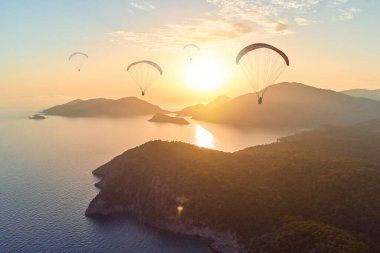 Gün batımında sisli deniz lagünündeki cennet gibi dağların arasında uçan bir grup yamaç paraşütçüsü. Yumuşak odaklı duvar kağıdı 