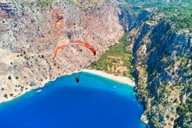 Güneşli yaz gününde mavi deniz koyundaki dağların arasında uçan paraglider manzarası 